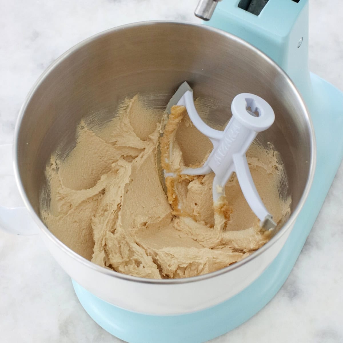 Creaming butter and brown sugar in a stand mixer to make soft raisin cookies.
