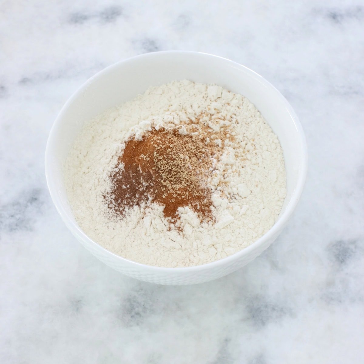 Mixing dry ingredients in a separate bowl, flour, baking powder and soda, cinnamon, nutmeg and allspice.