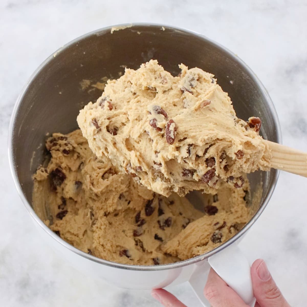 Mixing raisins into cookie dough in a bowl for soft raisin cookies.