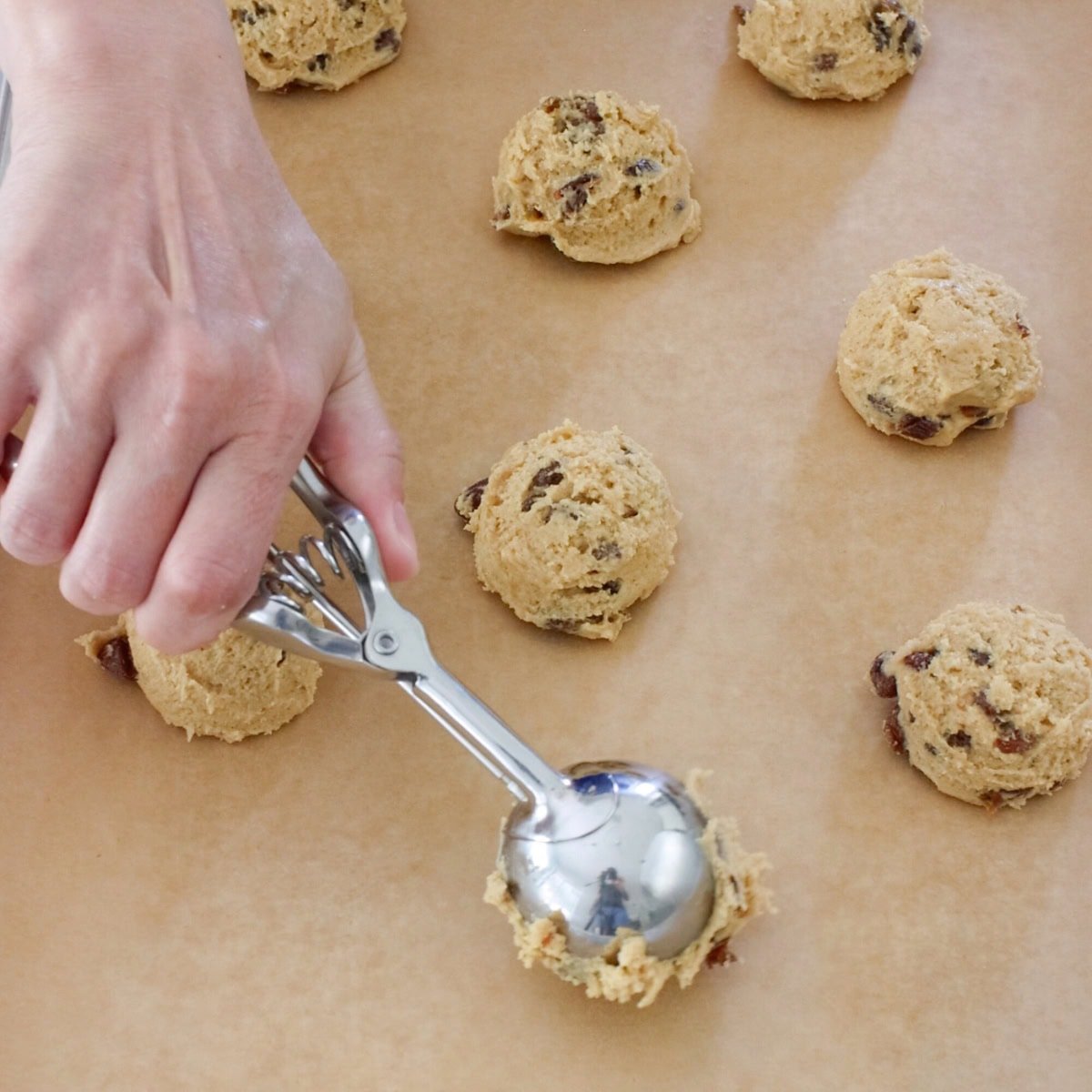 Scooping out soft raisin cookie batter onto baking sheet.