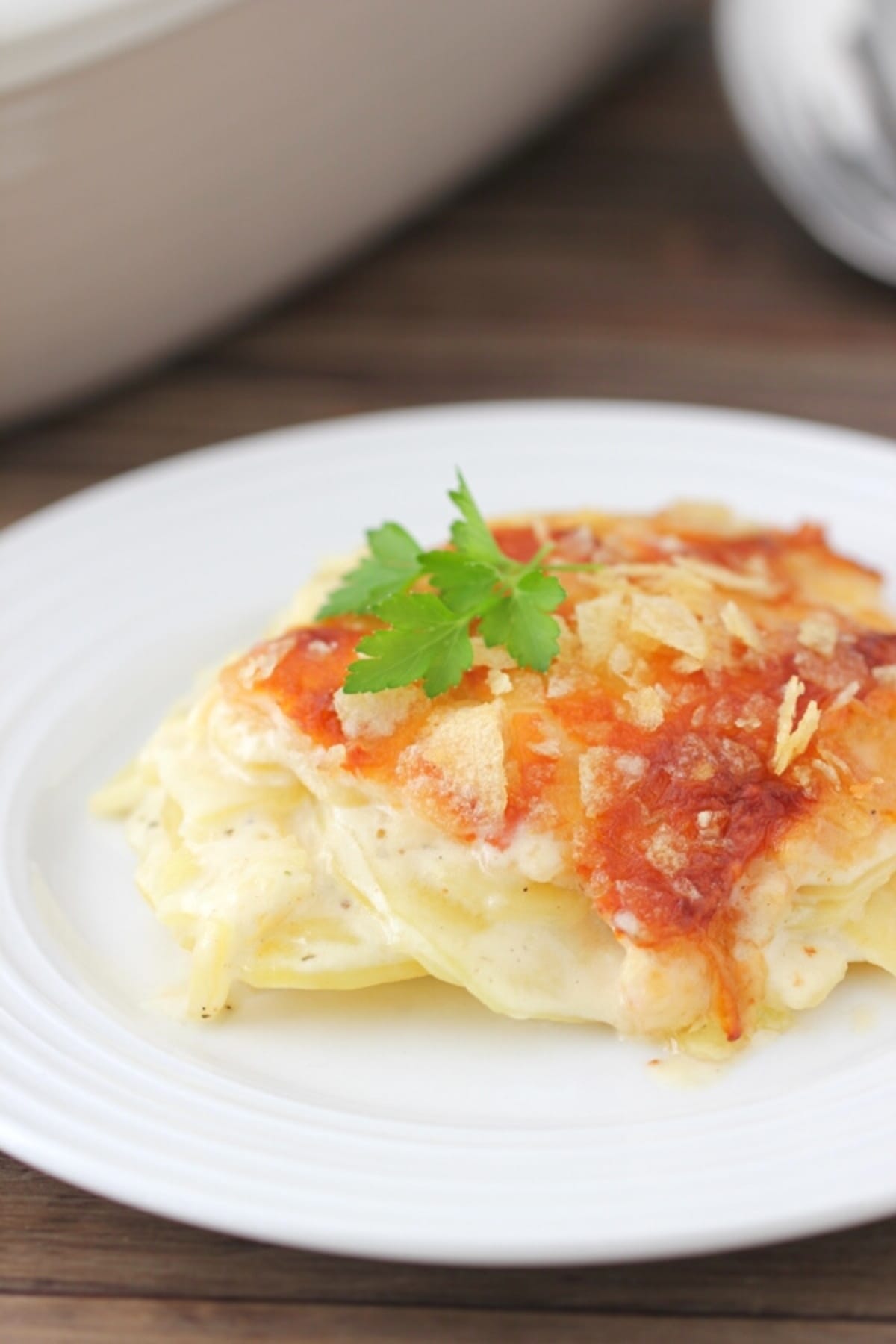 A serving of easy scalloped potatoes on a plate, with melted, golden cheese and crushed chips on top.