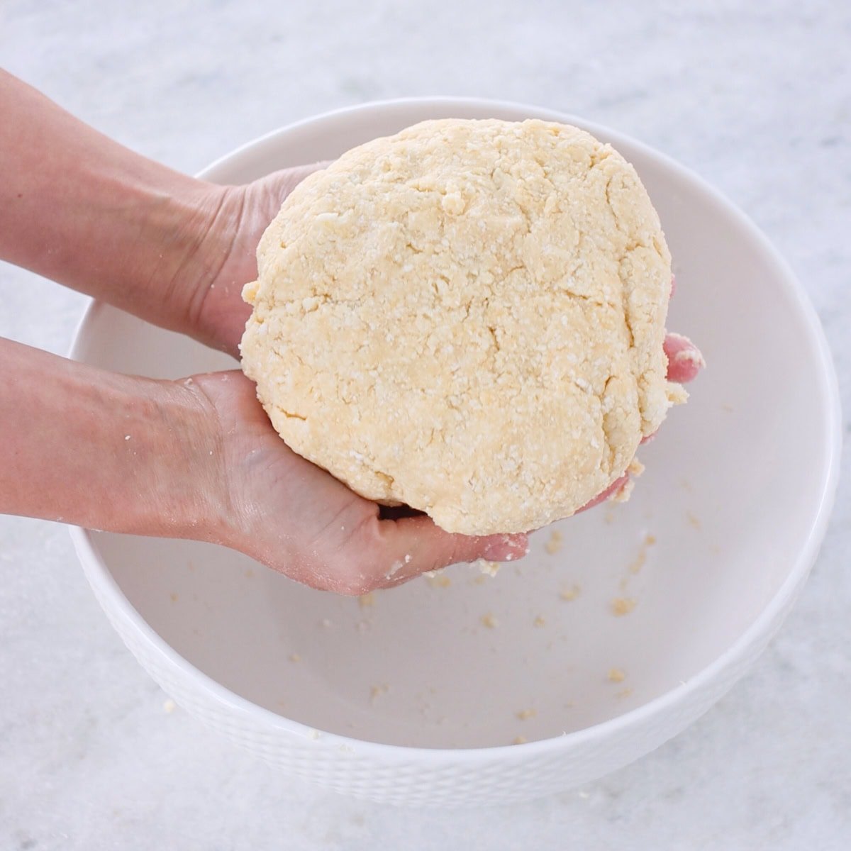 Farmer's cheese cookie dough made into a disc, held over the bowl.