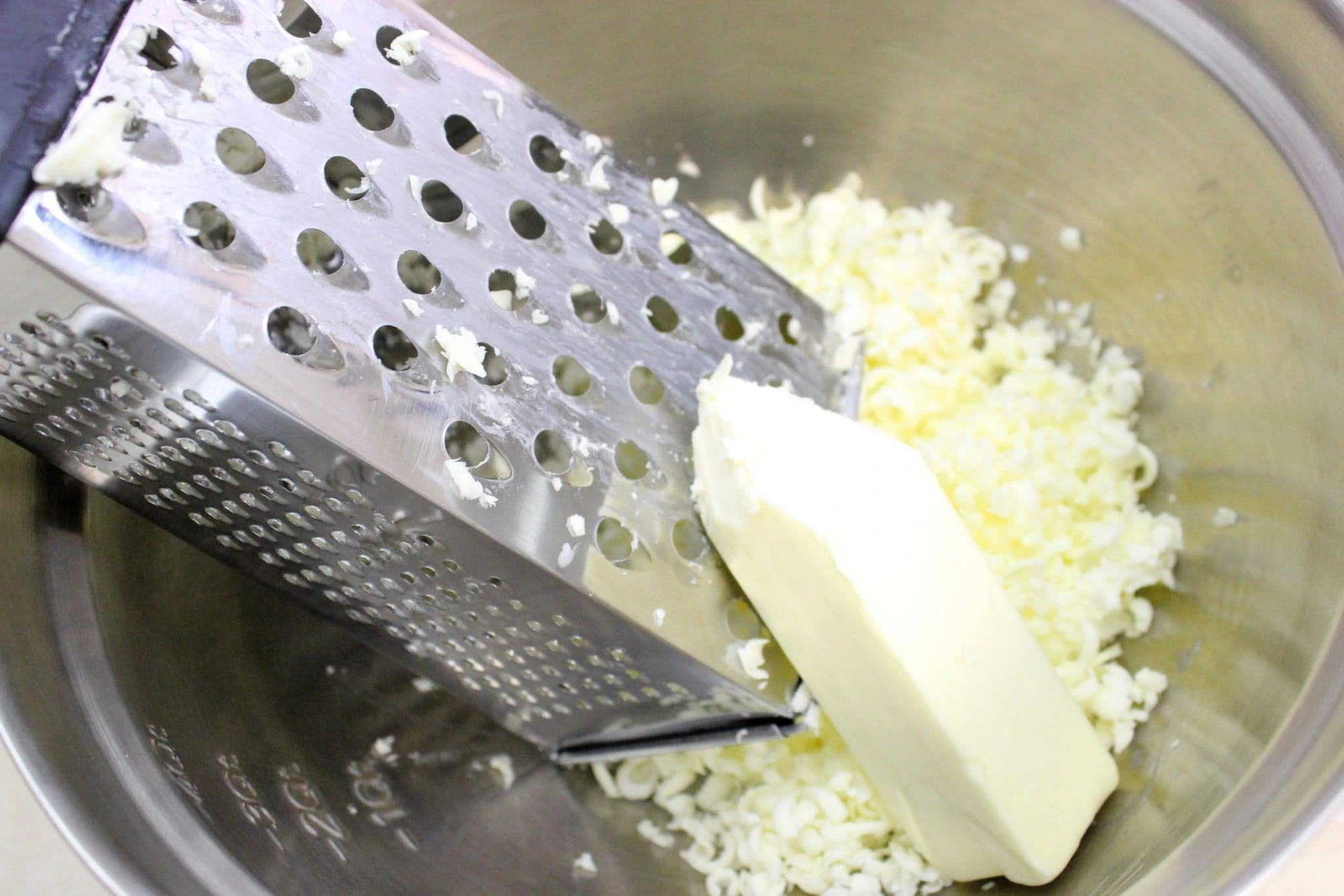 Grating frozen butter on a box grater for dough.