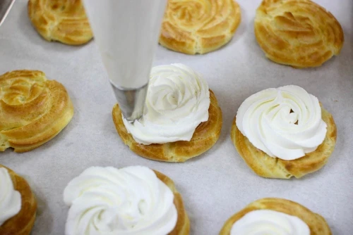 Piping whipped cream onto pastries