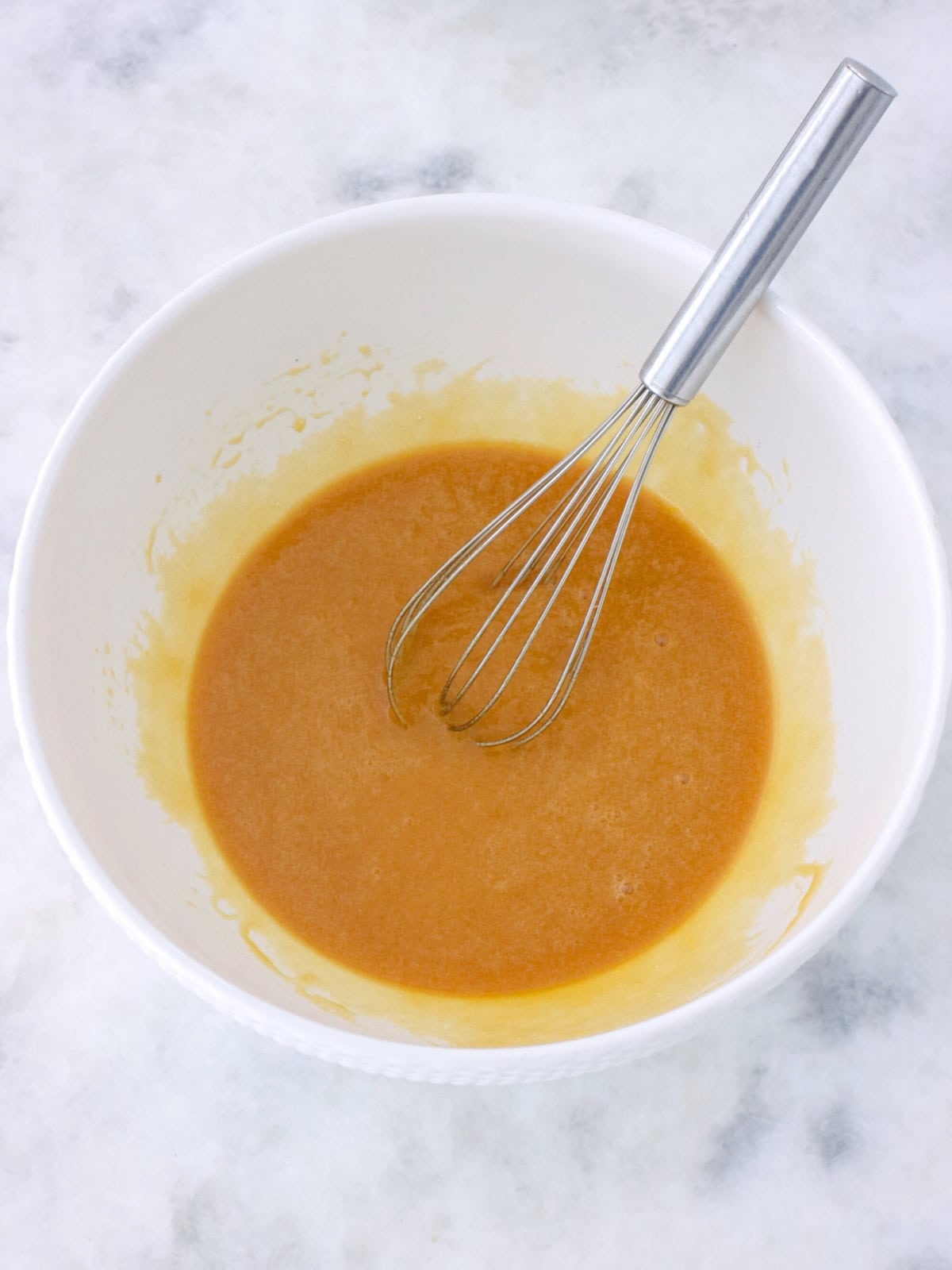 Liquid ingredients (butter, brown sugar, eggs and vanilla) whisked together in a bowl to make cookie bars. 