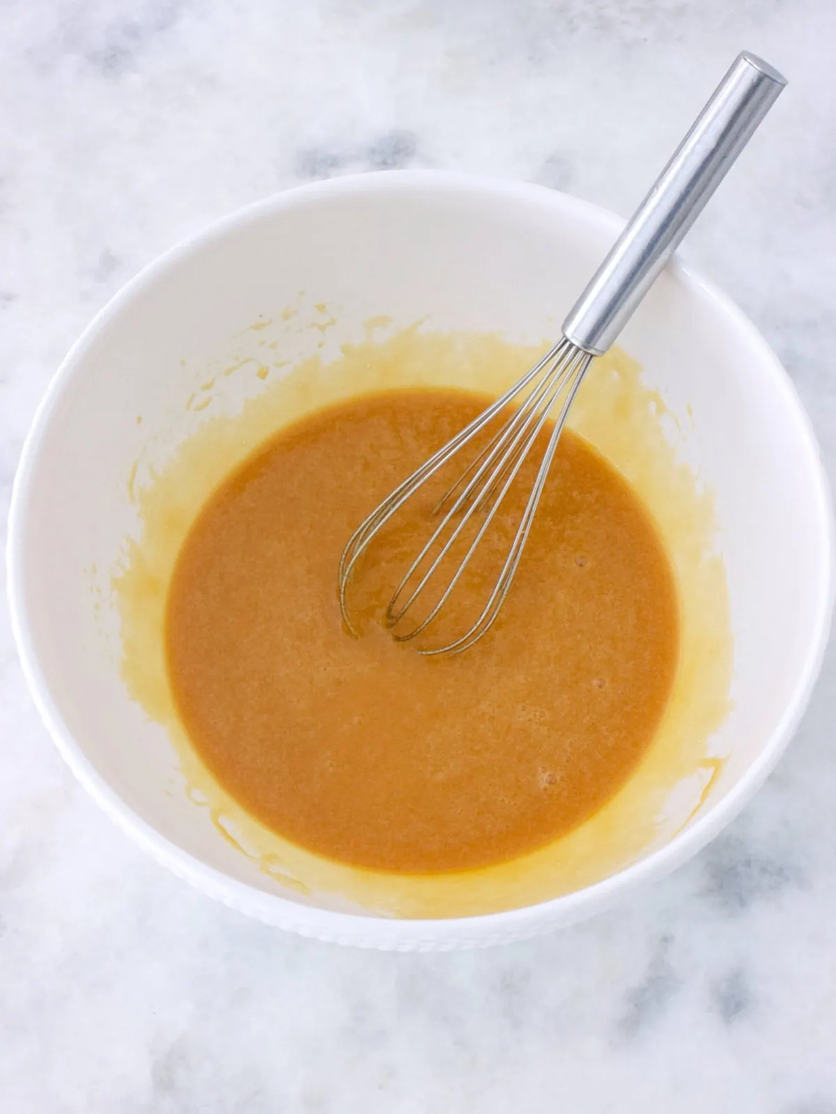 Liquid ingredients (butter, brown sugar, eggs and vanilla) whisked together in a bowl to make cookie bars.