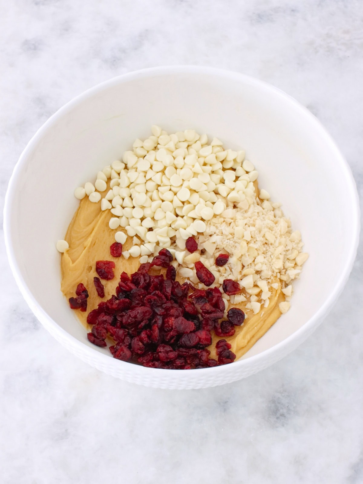 Cookie br batter in  bowl with white chocolate, cranberries and macadamia nuts. 
