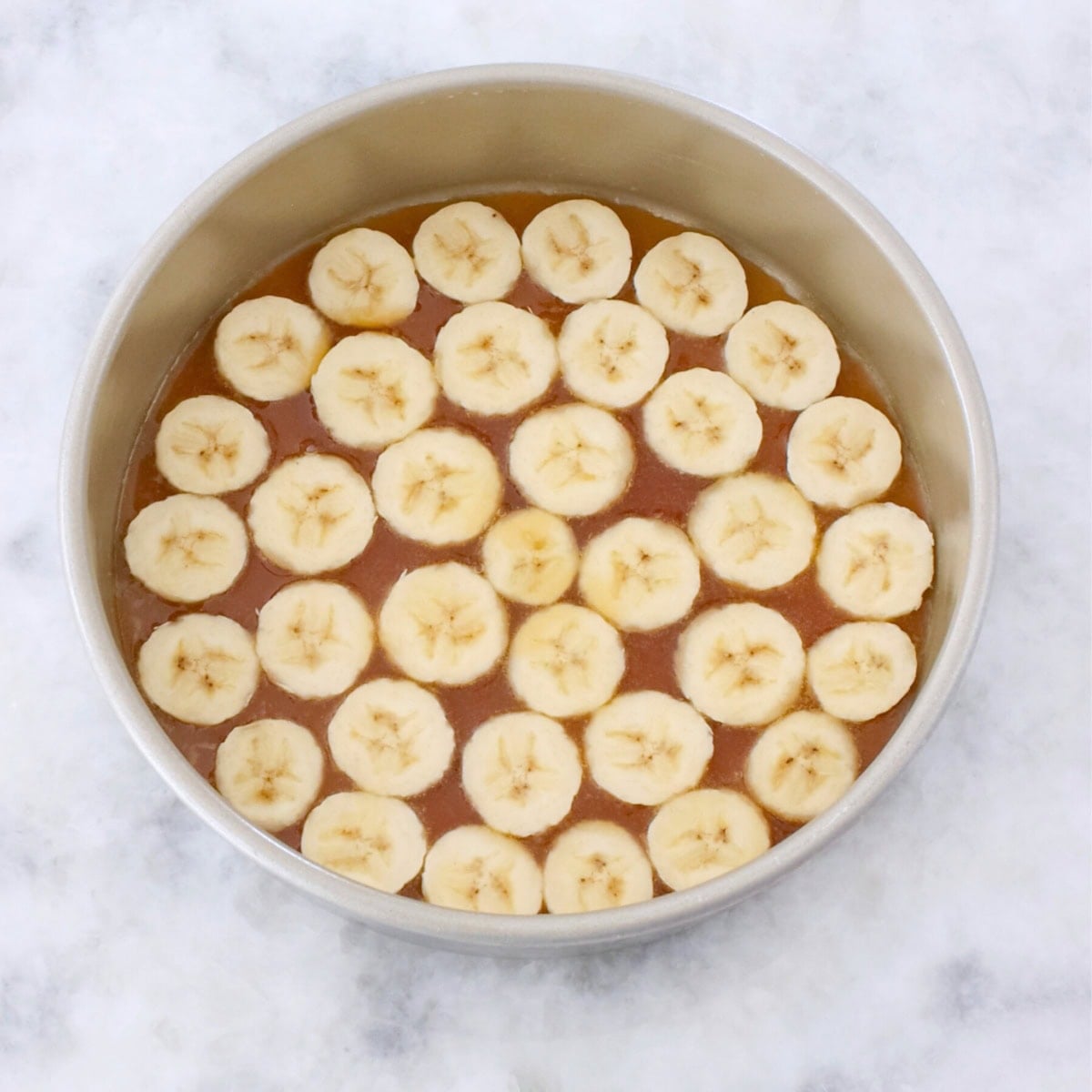 Banana upside down cake process shot, arranging sliced bananas in a cake pan.