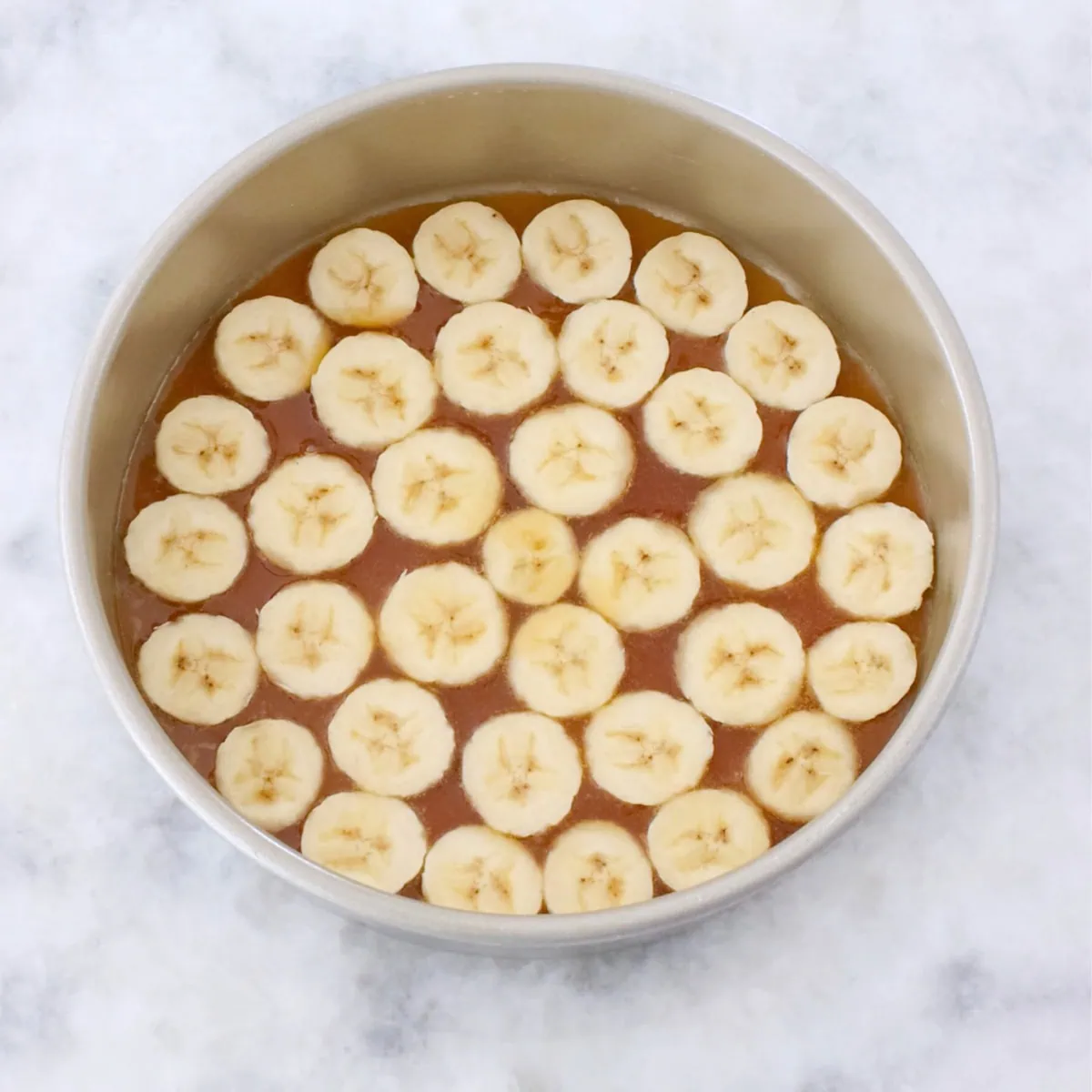 Banana upside down cake process shot, arranging sliced bananas in a cake pan. 