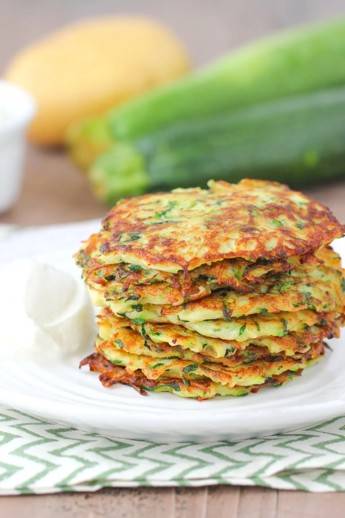 Zucchini and Potato Fritters stacked up on a plate with sour cream on the side.