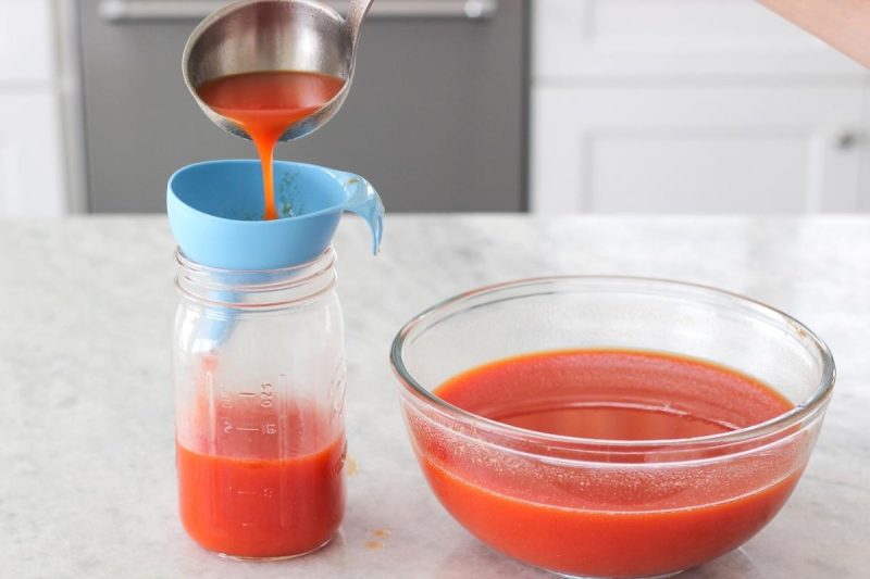 Pouring homemade tomato juice into jars using a funnel. 