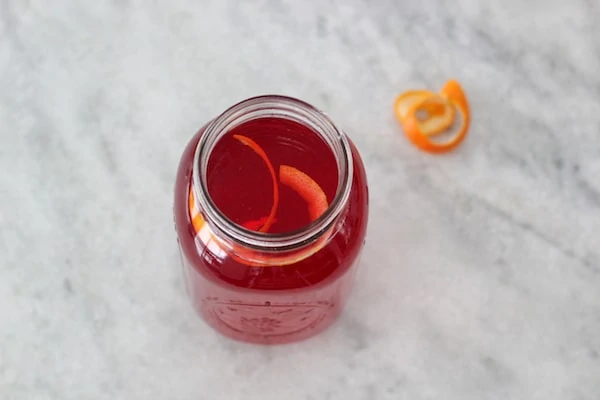 Cranberry raspberry drink in a mason jar with clementine peel on a counter. 