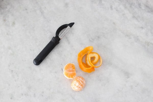 Clementine fruit and peel with a vegetable peeler laying on a marble countertop. 