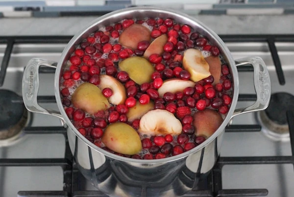 Cranberries, raspberries and apples for Kompot cooking in a stockpot on a gas cooktop. 