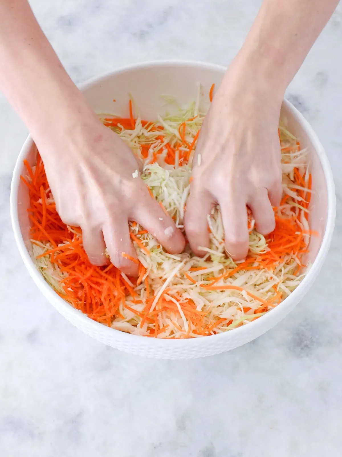 Making homemade sauerkraut in a large bowl, mixing and massaging the cabbage and carrot. 