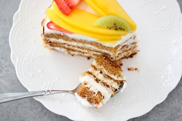 A slice of fluffy honey layer cake, a spoonful of cake and sour cream frosting with fruit on top.