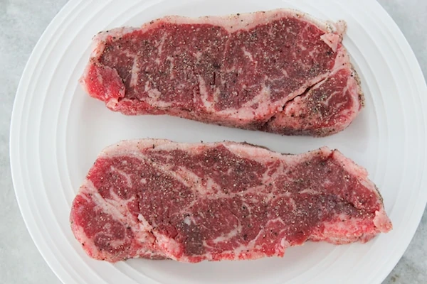 Seasoned steaks on a plate, salt and coarsely ground black pepper