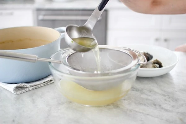 Clear fish broth prepared from a whole fish to make Ukha fish soup, straining through a sieve 