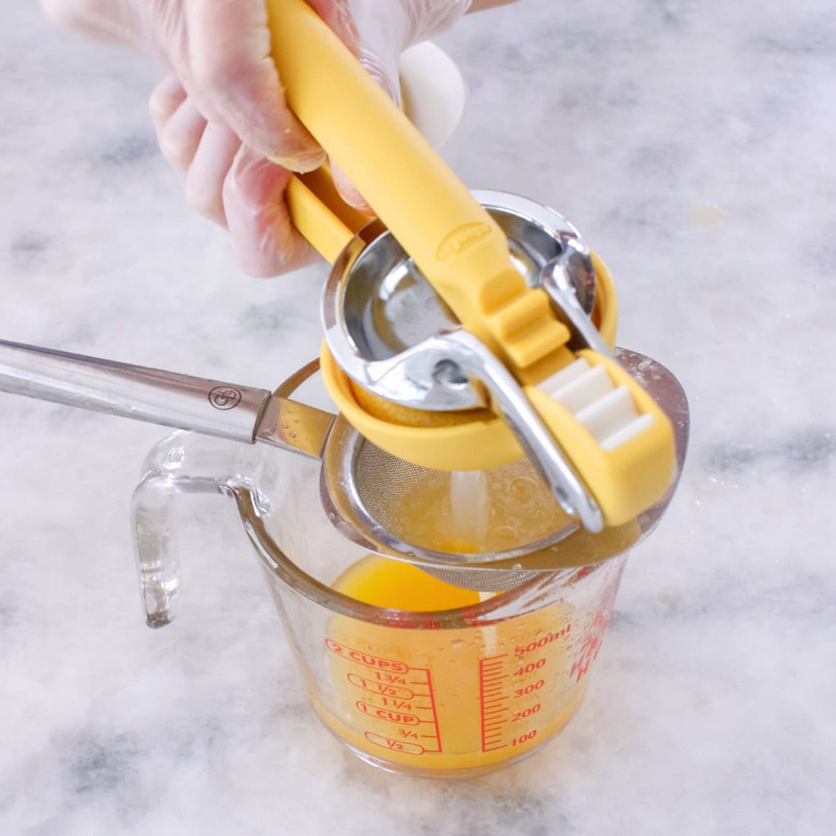 Freshly squeezed orange juice and lemon juice in a glass measuring cup. Citrus juicer squeezing out lemon juice.