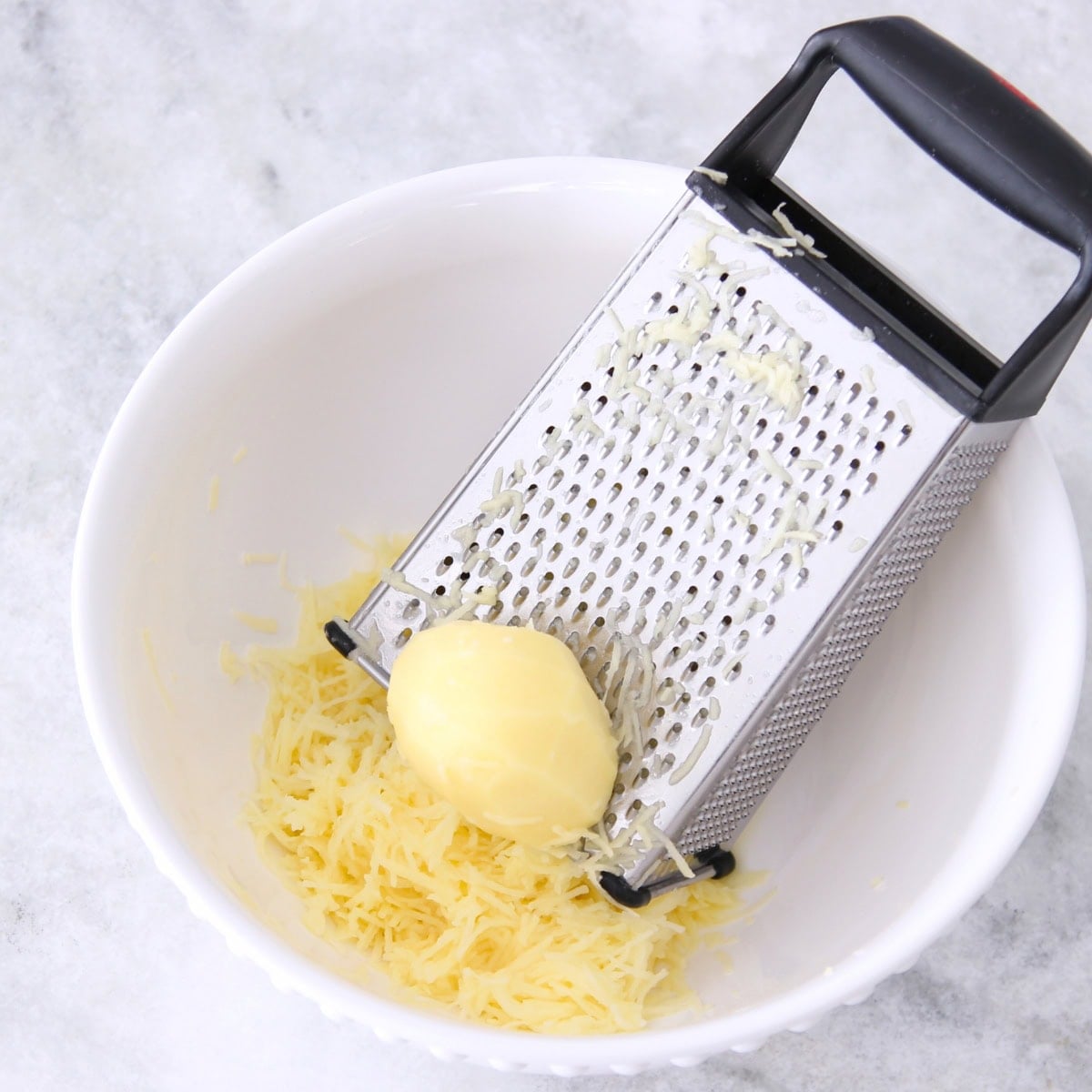 Potato waffles process shot, grating potatoes on box grater into bowl. 