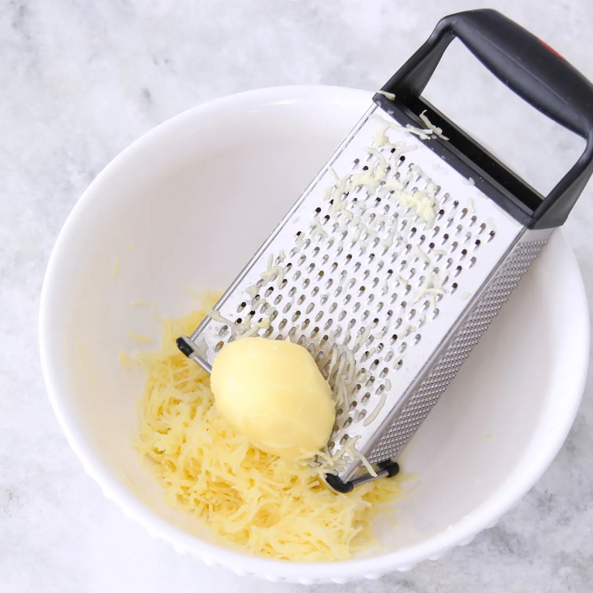 Potato waffles process shot, grating potatoes on box grater into bowl. 