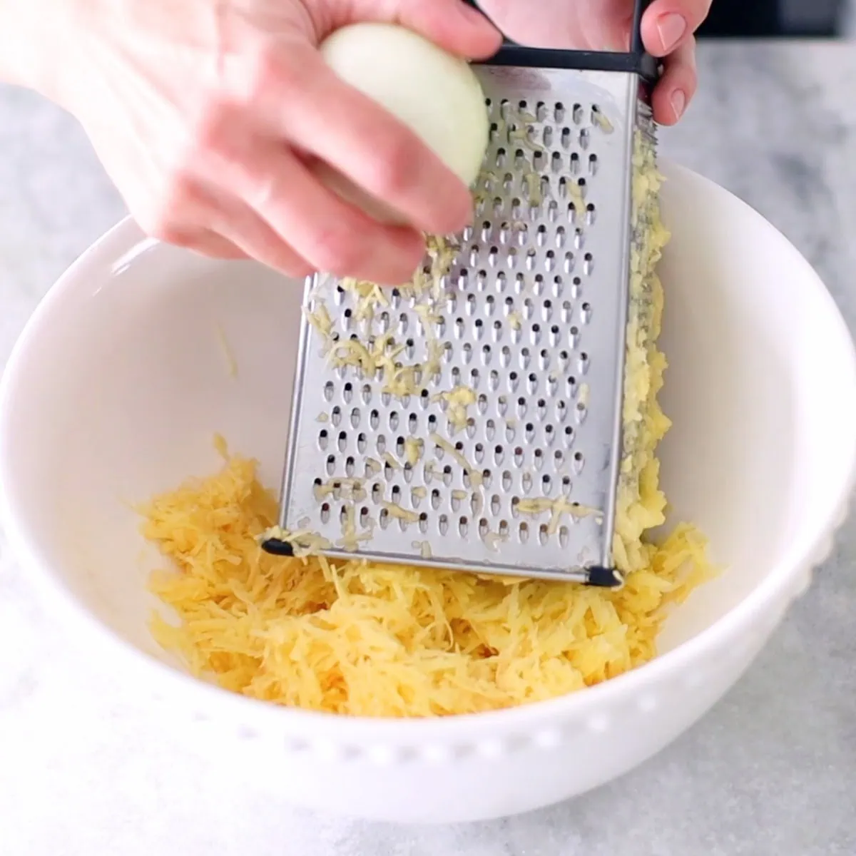 Grating onion on box grater into a bowl for potato waffles. 