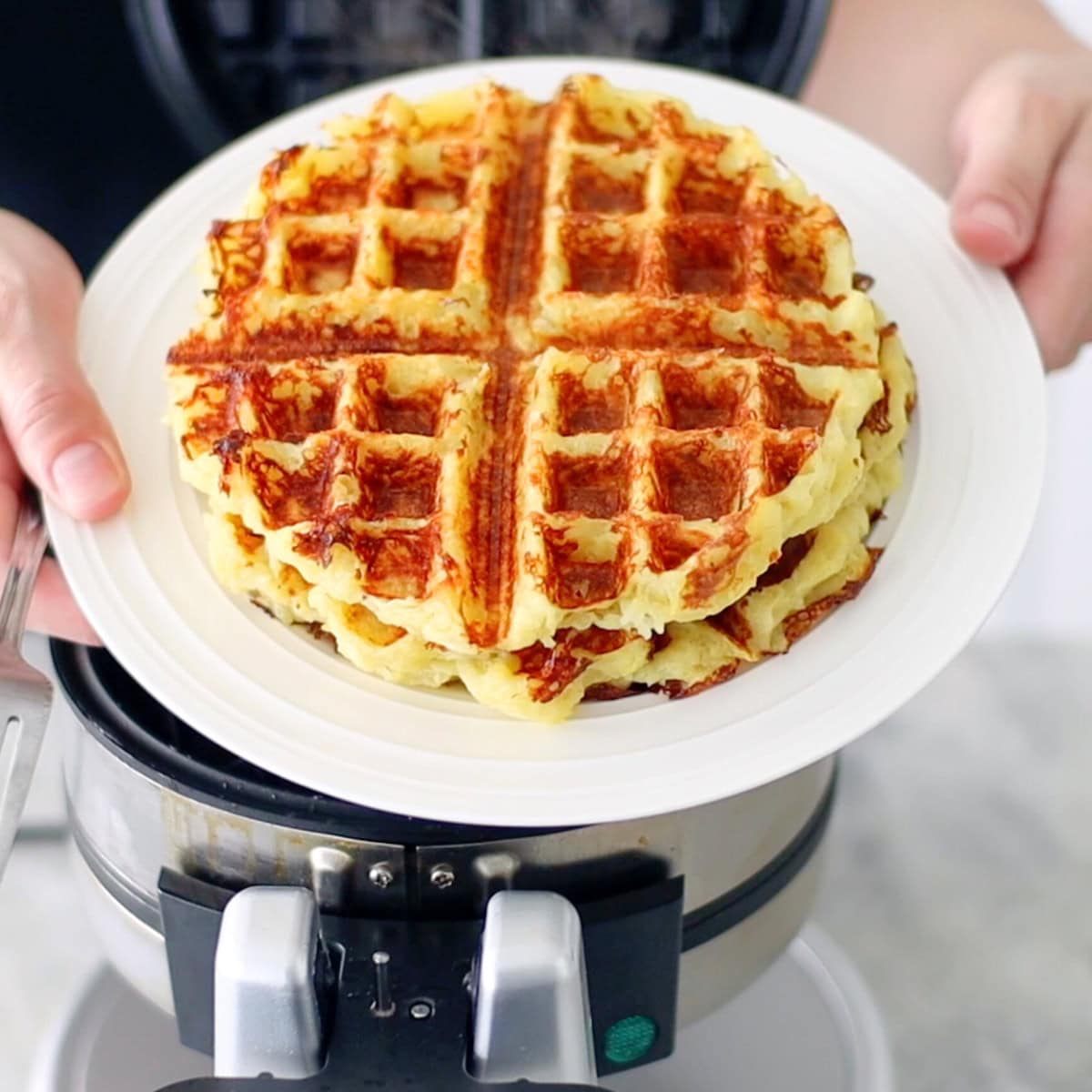 Golden brown potato waffles on a plate, right after being cooked in a waffle maker. 