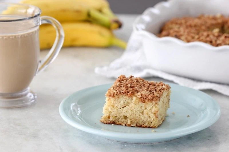 A slice of banana coffee cake with a streusel topping served with a cup of coffee