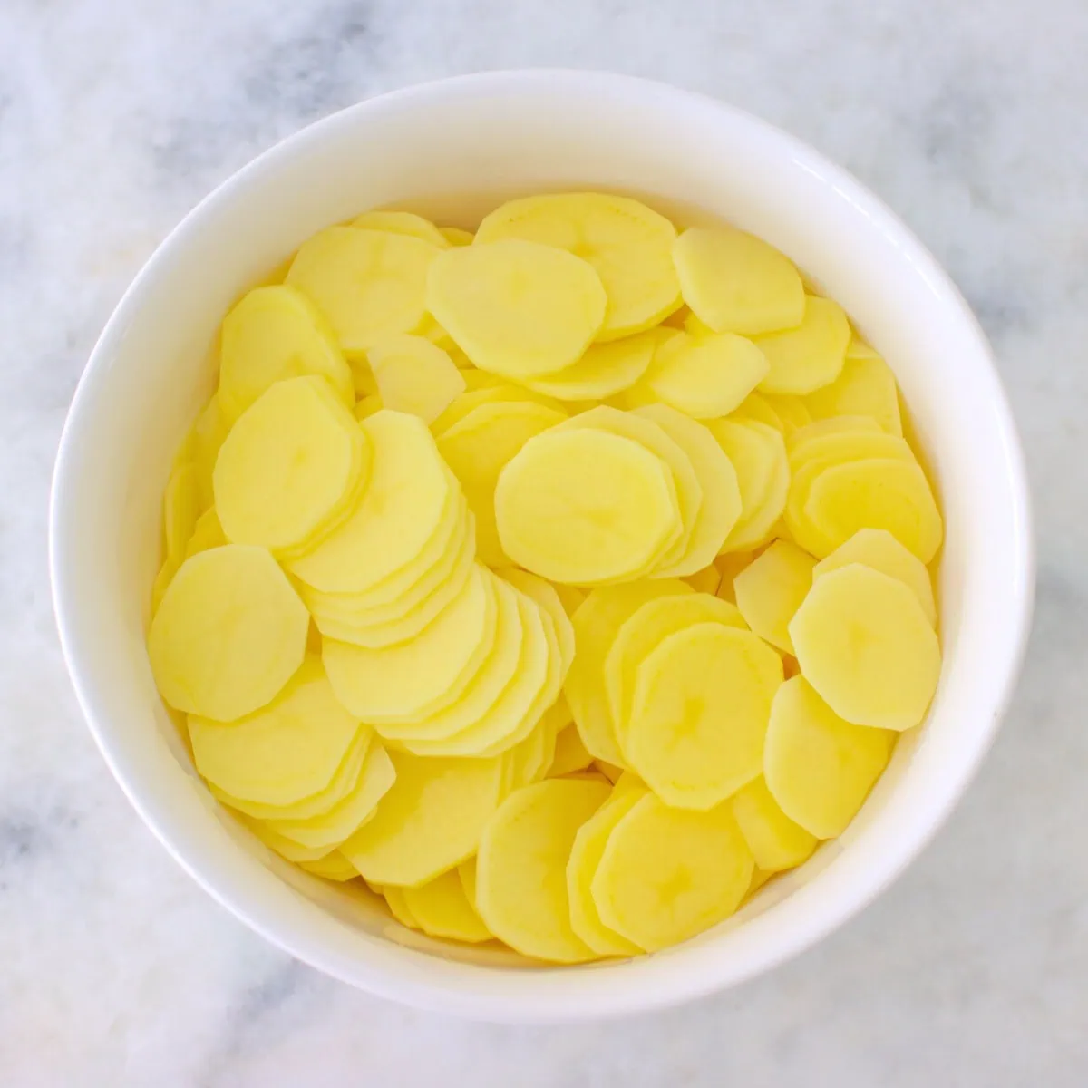 Thinly sliced gold potatoes in a bowl for scalloped potatoes. 