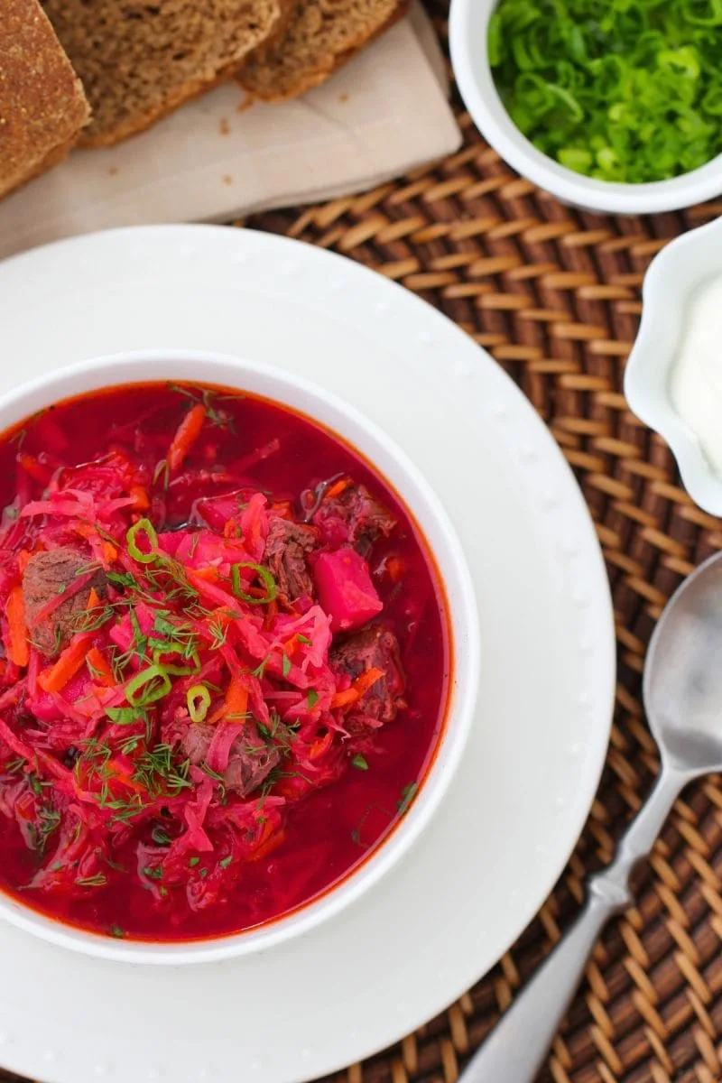 A bowl of Beet Borsch - made with beef, potatoes, beets, carrots, onions and served with sour cream and fresh herbs. 