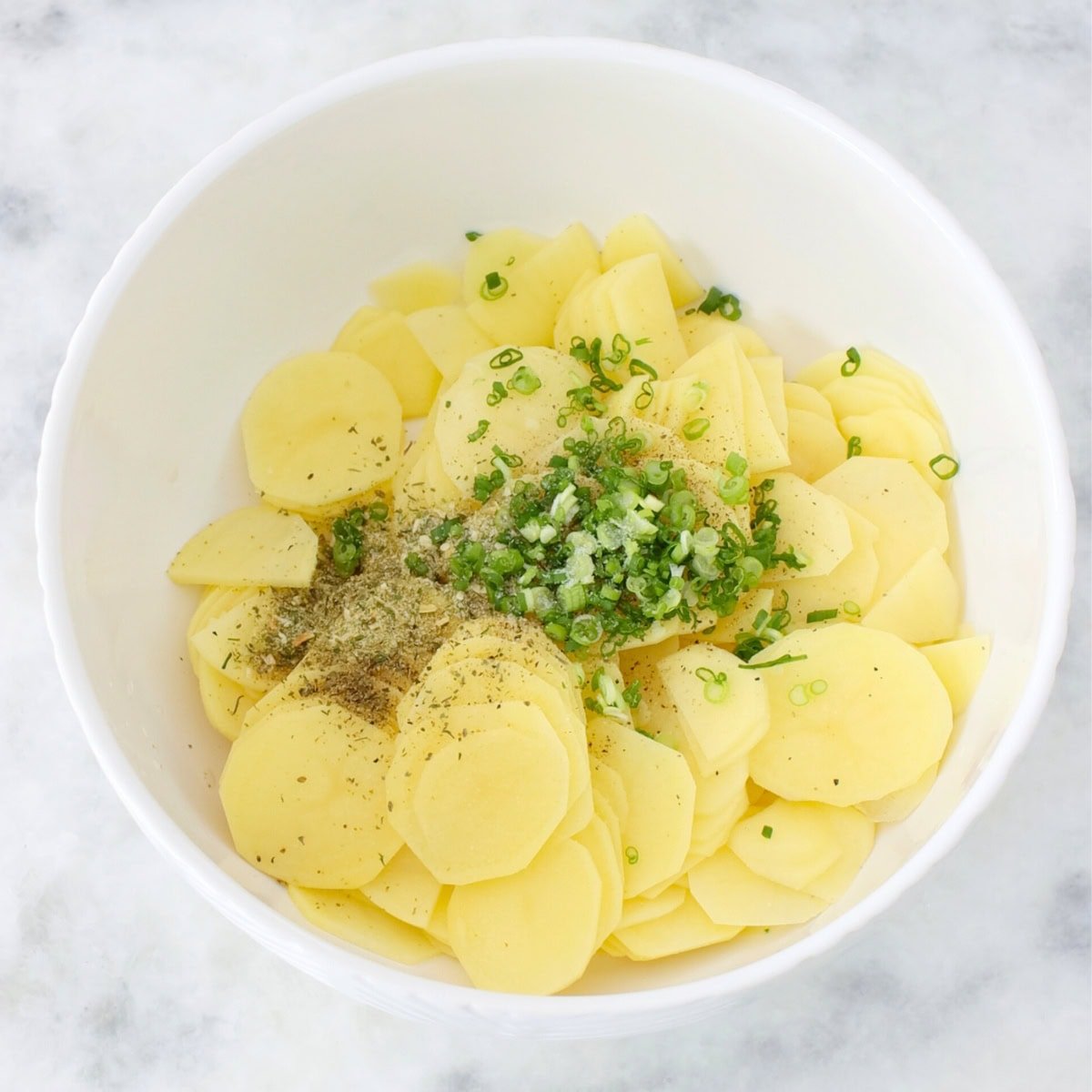 Thinly sliced potatoes in a bowl with herbs and spices to be used in a potato pastry. 