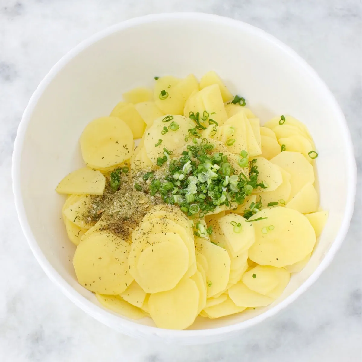 Thinly sliced potatoes in a bowl with herbs and spices to be used in a potato pastry. 