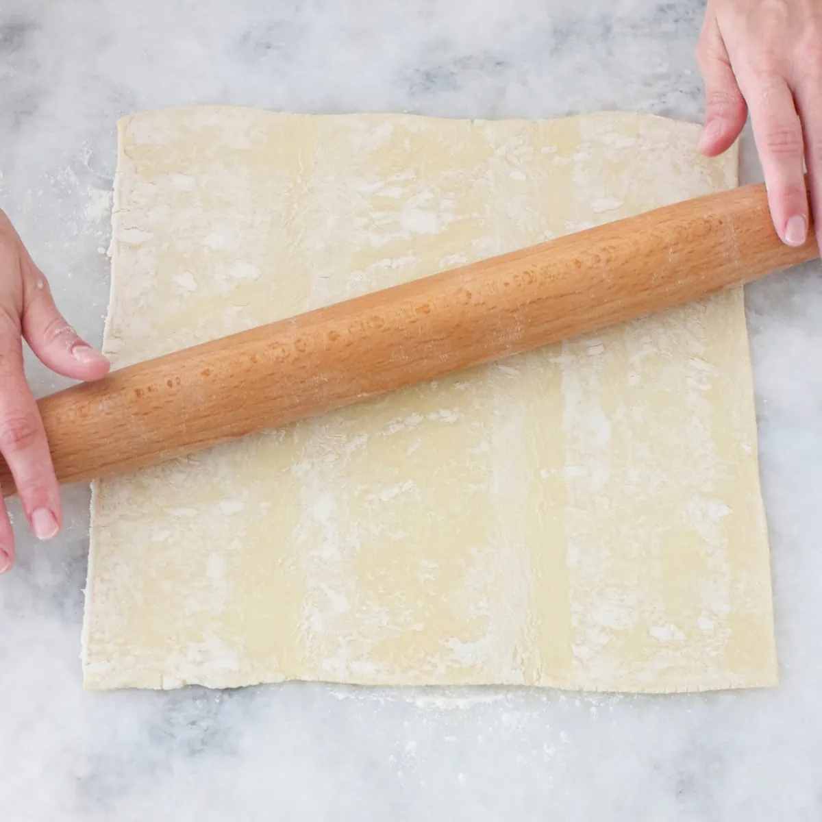 Frozen/thawed puff pastry rolled out with a rolling pin on a counter. 