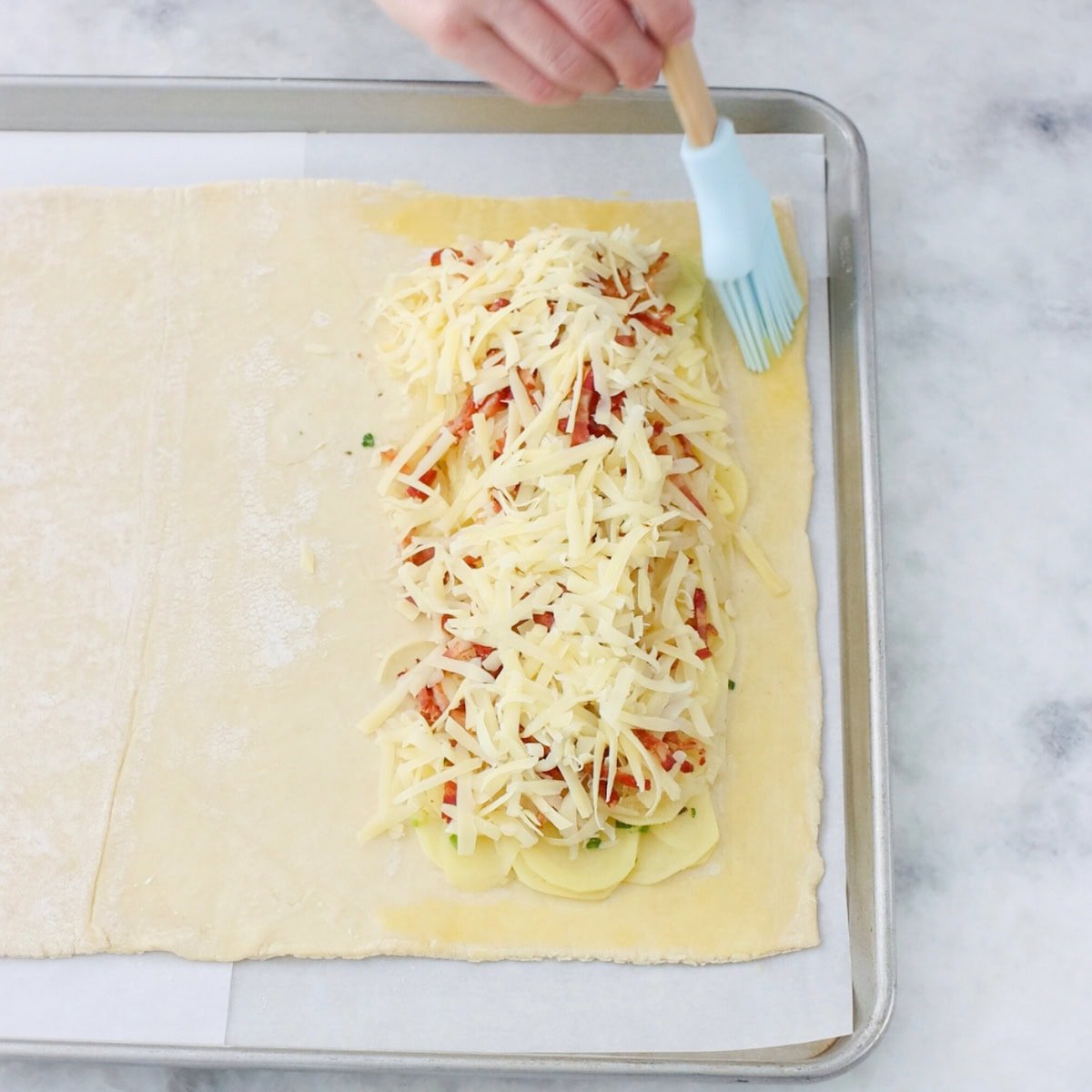 Assembling a potato bacon pastry, brushing egg wash around the edges. 