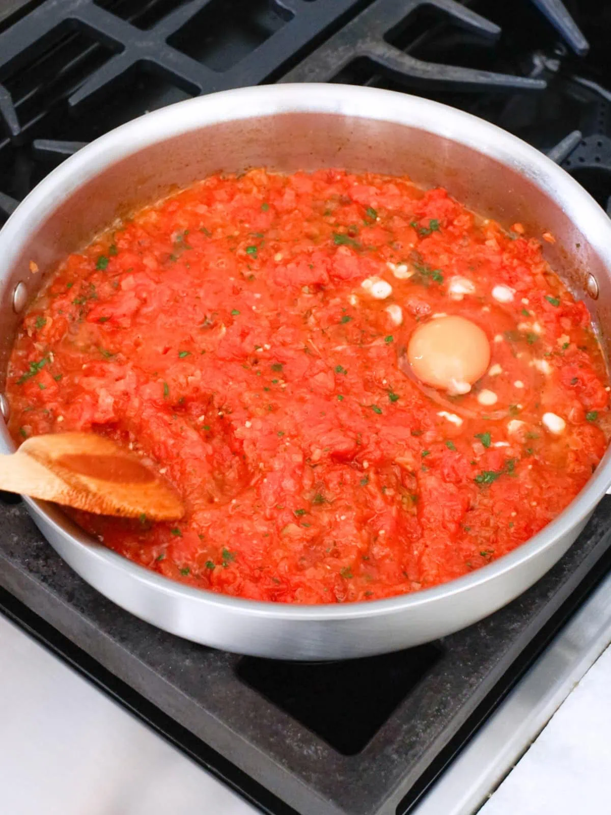 Eggs being added to tomatoes in a deep skillet for Shakshuka. 