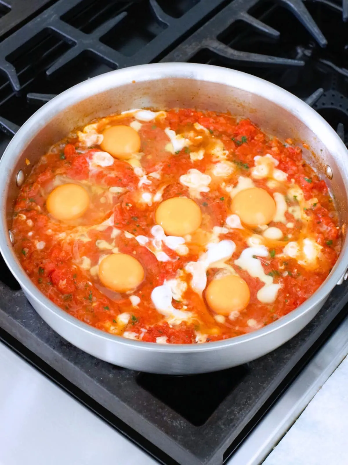Eggs cooked in tomato mixture in a deep skillet for Shakshuka with fresh tomatoes. 